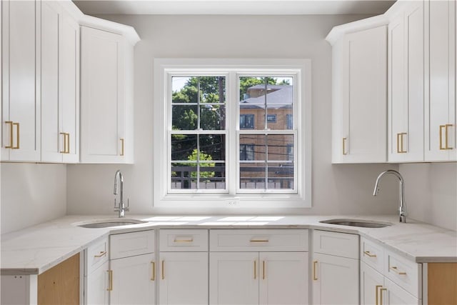 kitchen featuring white cabinets, light stone counters, and sink