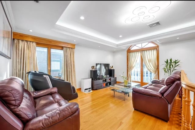 living room featuring ornamental molding, a tray ceiling, and light hardwood / wood-style flooring