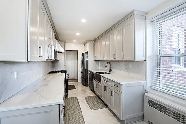 kitchen featuring decorative backsplash, appliances with stainless steel finishes, light stone counters, sink, and radiator heating unit