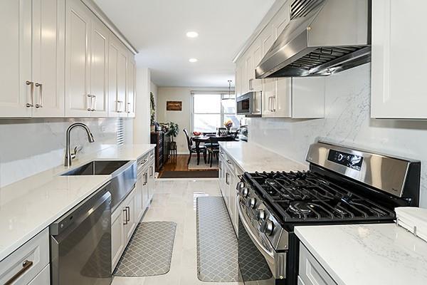 kitchen featuring light stone countertops, sink, wall chimney exhaust hood, stainless steel appliances, and decorative backsplash