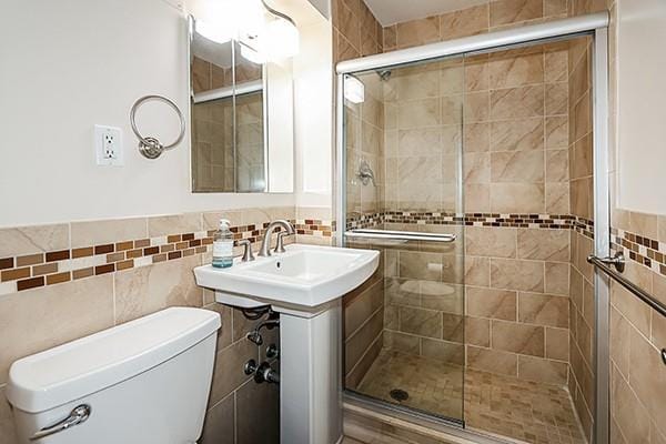 bathroom with toilet, a shower with door, and tile walls