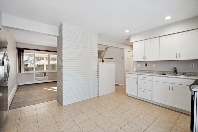 kitchen with light tile patterned flooring, sink, white cabinets, light stone countertops, and a wall unit AC