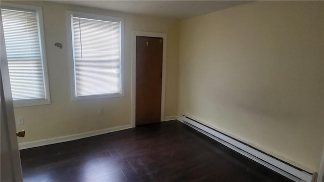 unfurnished room featuring baseboard heating and dark wood-type flooring