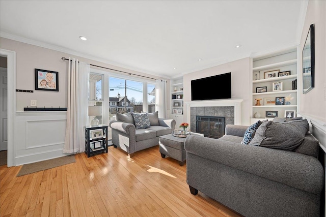 living room featuring built in shelves, crown molding, light hardwood / wood-style flooring, and a tiled fireplace