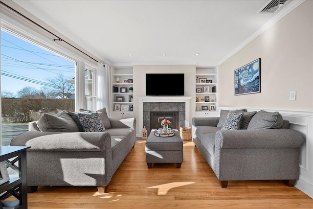 living room featuring a fireplace, built in shelves, ornamental molding, and hardwood / wood-style floors