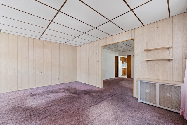 carpeted spare room with radiator, a paneled ceiling, and wood walls