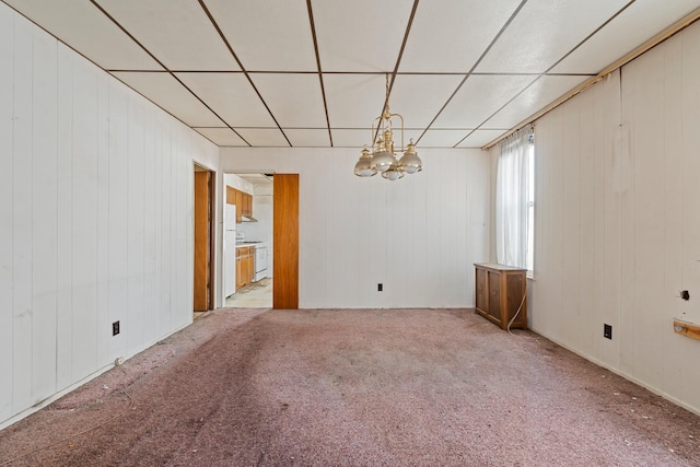 carpeted empty room featuring a drop ceiling, a notable chandelier, and wooden walls