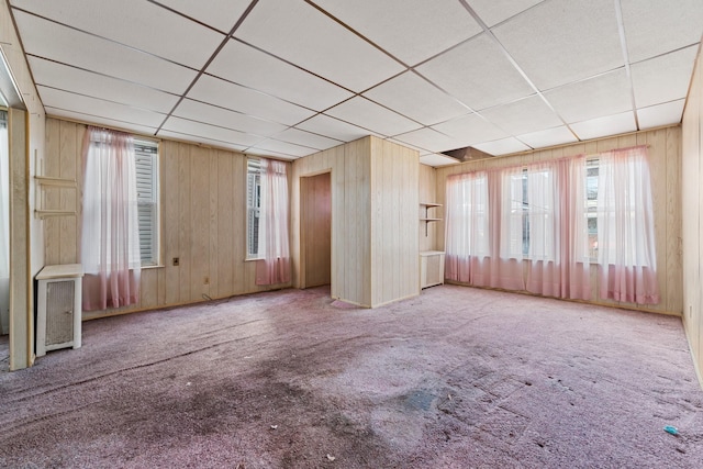 miscellaneous room featuring light colored carpet, a drop ceiling, radiator heating unit, and wooden walls