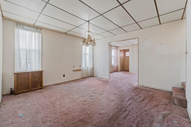 interior space featuring wood walls, a chandelier, light colored carpet, and a drop ceiling