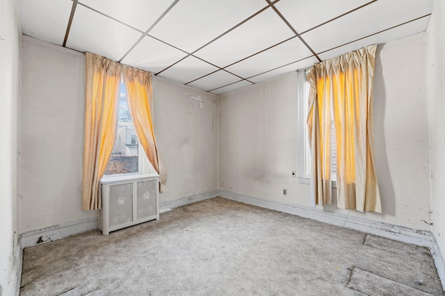 empty room with radiator, carpet flooring, and a drop ceiling