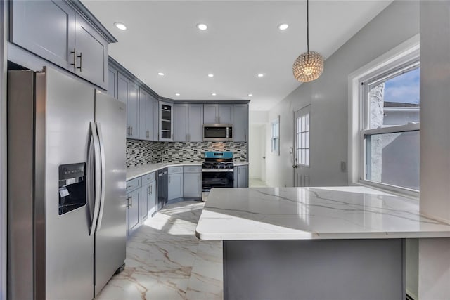 kitchen with appliances with stainless steel finishes, light stone counters, hanging light fixtures, and gray cabinetry