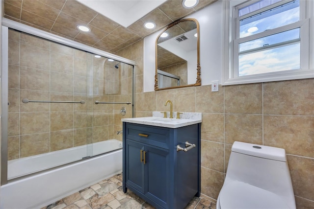 full bathroom featuring vanity, toilet, tile walls, and bath / shower combo with glass door