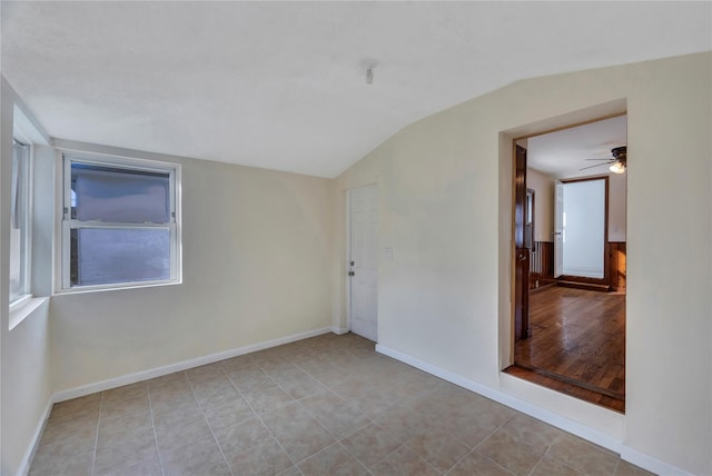 empty room featuring ceiling fan, light tile patterned floors, a healthy amount of sunlight, and vaulted ceiling