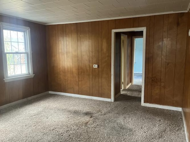 spare room featuring carpet, crown molding, and wooden walls