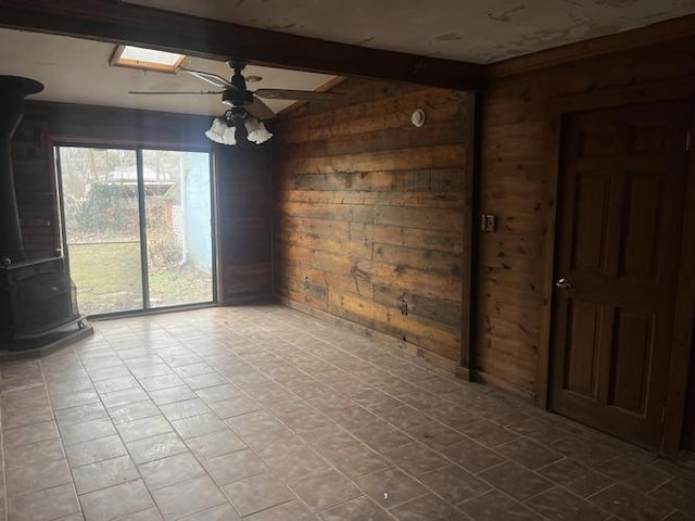 unfurnished dining area with a skylight, a wood stove, ceiling fan, beamed ceiling, and wooden walls