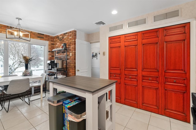 kitchen with an inviting chandelier, light tile patterned floors, brick wall, and hanging light fixtures