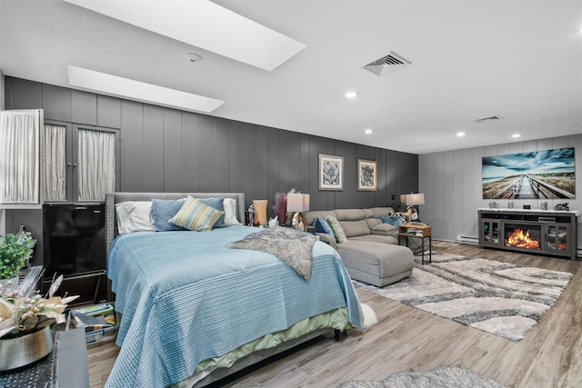 bedroom with a baseboard heating unit, light hardwood / wood-style flooring, a skylight, and a fireplace