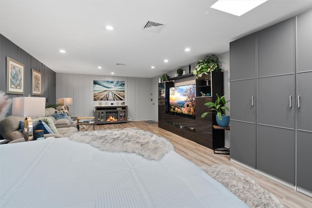 bedroom with light wood-type flooring, a fireplace, and a skylight