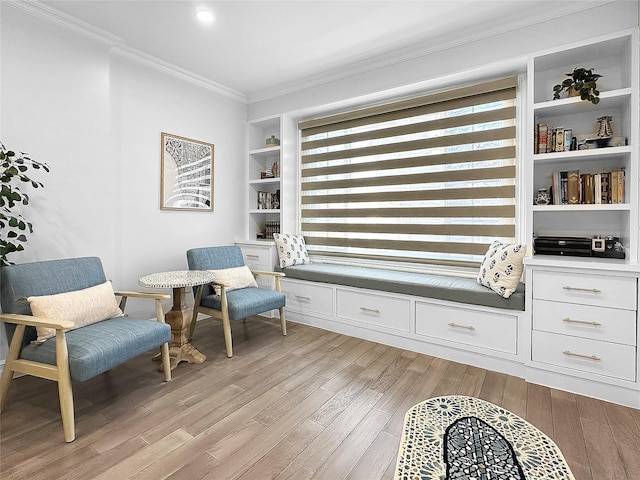 living area with built in shelves, light wood-type flooring, and ornamental molding