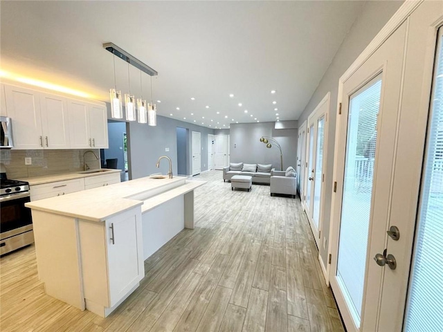 kitchen with a center island with sink, light hardwood / wood-style floors, stainless steel appliances, white cabinetry, and decorative light fixtures