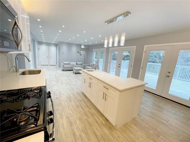 kitchen featuring hanging light fixtures, french doors, gas range oven, white cabinets, and sink