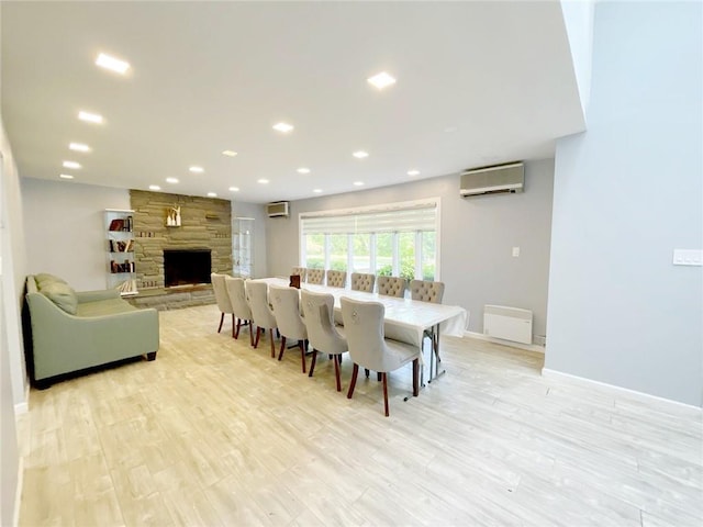 dining area featuring a wall unit AC, light wood-type flooring, and a stone fireplace