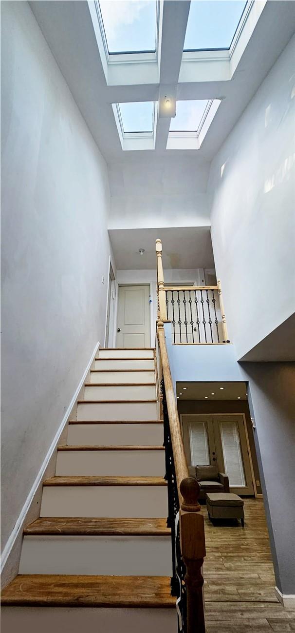 staircase featuring a towering ceiling, wood-type flooring, and a skylight