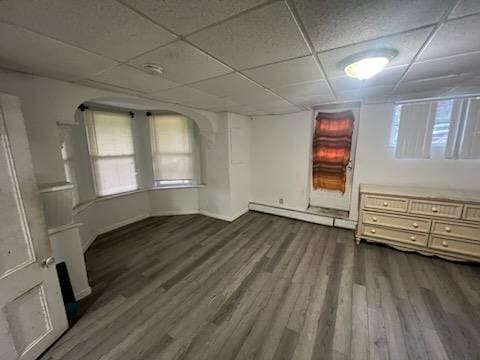 empty room with dark hardwood / wood-style flooring, a baseboard radiator, and a drop ceiling