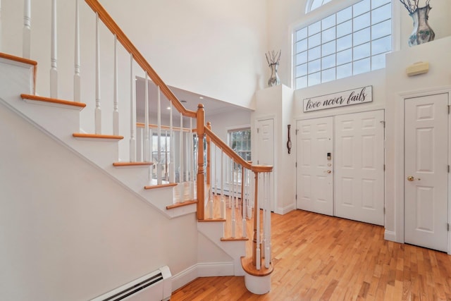 entrance foyer featuring a baseboard heating unit, a high ceiling, and light wood-type flooring