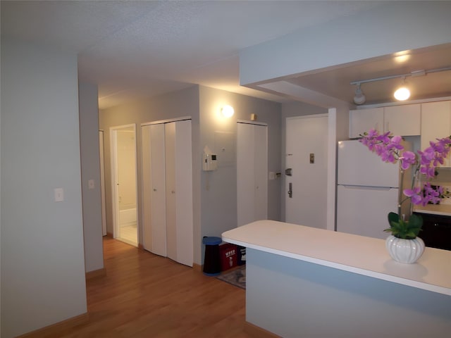 kitchen featuring white cabinets, light wood-type flooring, white fridge, and kitchen peninsula