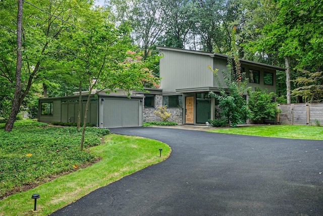 mid-century modern home featuring aphalt driveway, stone siding, fence, and an attached garage