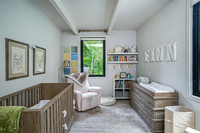 carpeted bedroom featuring beamed ceiling and a crib