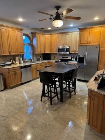 kitchen with a center island, sink, ceiling fan, appliances with stainless steel finishes, and a breakfast bar area