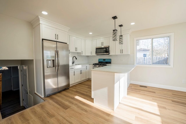 kitchen featuring pendant lighting, sink, kitchen peninsula, white cabinetry, and stainless steel appliances