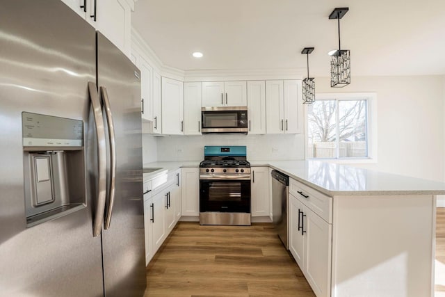 kitchen with hardwood / wood-style floors, white cabinetry, hanging light fixtures, and stainless steel appliances