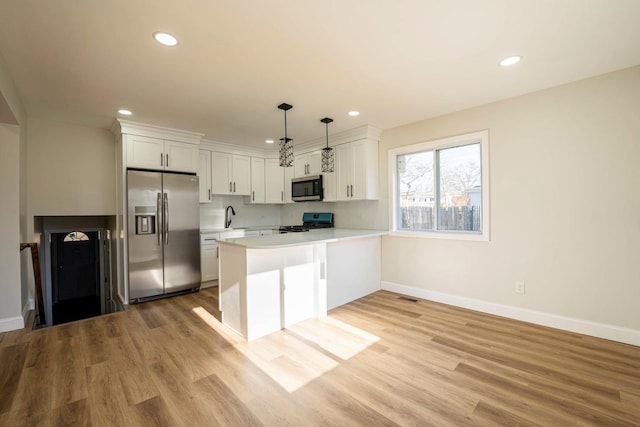 kitchen featuring stainless steel appliances, light hardwood / wood-style flooring, kitchen peninsula, pendant lighting, and white cabinets