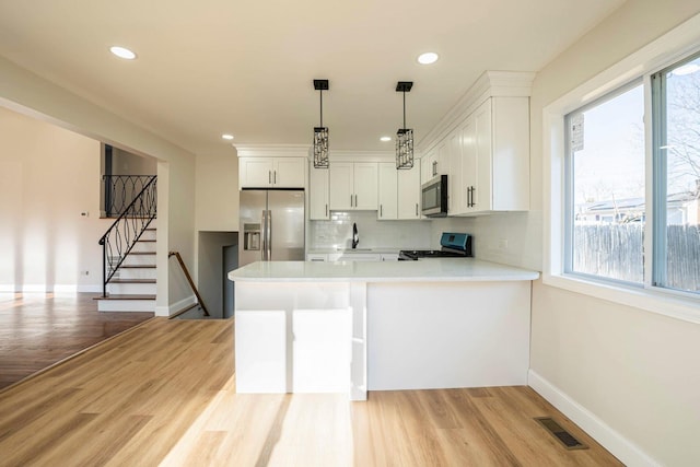 kitchen with white cabinetry, stainless steel appliances, kitchen peninsula, light hardwood / wood-style floors, and decorative light fixtures