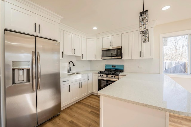 kitchen with white cabinets, sink, hanging light fixtures, appliances with stainless steel finishes, and kitchen peninsula