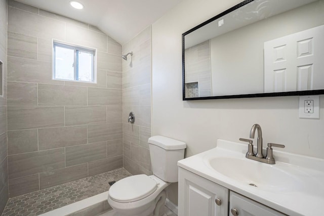 bathroom with toilet, a tile shower, vanity, and vaulted ceiling