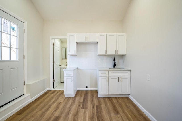 kitchen with light wood-type flooring, backsplash, white cabinetry, and sink