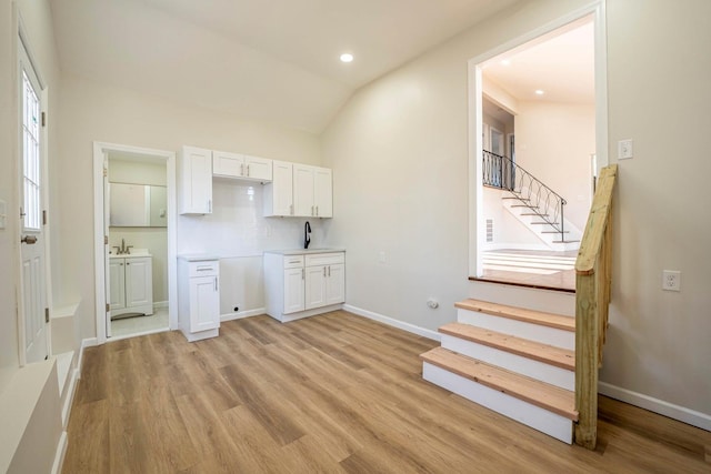 kitchen with white cabinets, vaulted ceiling, light hardwood / wood-style flooring, and tasteful backsplash