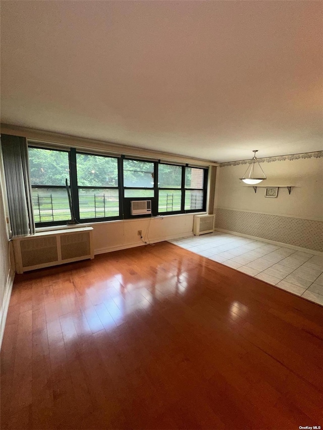 empty room with a wall unit AC, radiator heating unit, and light hardwood / wood-style floors