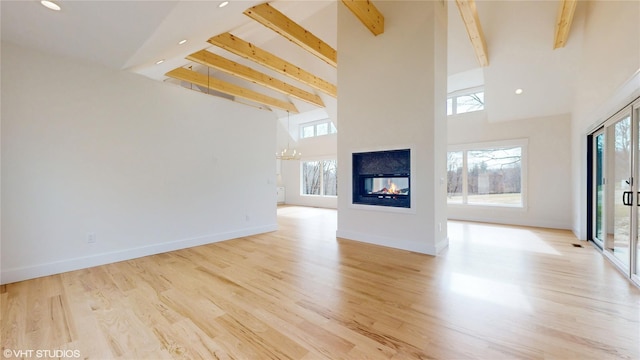 unfurnished living room with light wood-style floors, a wealth of natural light, beam ceiling, and a multi sided fireplace