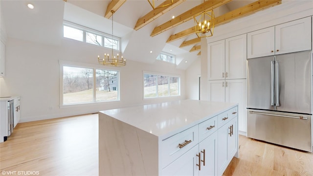 kitchen with a notable chandelier, stainless steel appliances, white cabinets, light wood-type flooring, and beamed ceiling