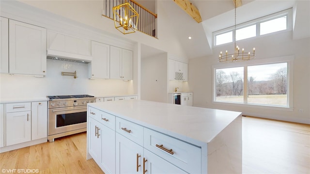 kitchen with stainless steel gas stove, a notable chandelier, premium range hood, and white cabinetry