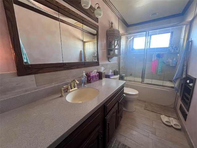 full bathroom featuring vanity, backsplash, combined bath / shower with glass door, crown molding, and toilet