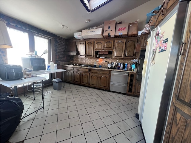 kitchen featuring tasteful backsplash, wall chimney exhaust hood, vaulted ceiling with skylight, dark brown cabinets, and light tile patterned floors