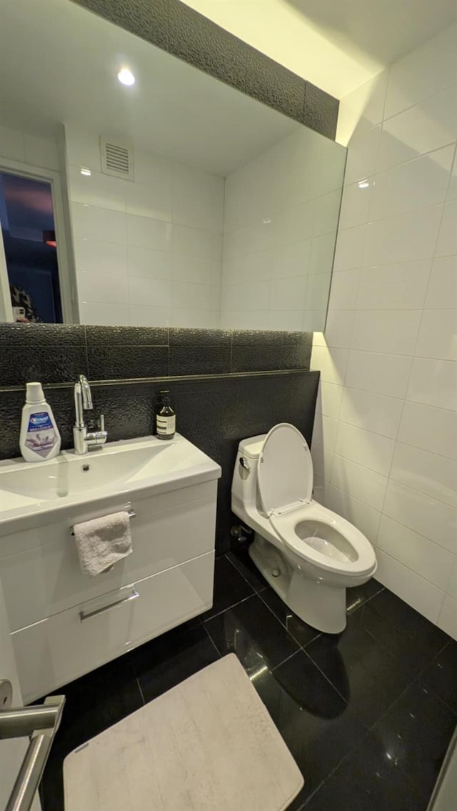 bathroom with toilet, tile patterned flooring, tile walls, and vanity