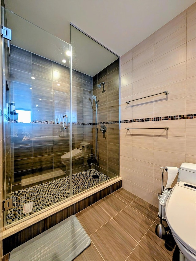 bathroom with a shower with shower door, tile patterned floors, toilet, and tile walls