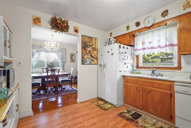 kitchen featuring white appliances, sink, decorative light fixtures, a notable chandelier, and light hardwood / wood-style floors